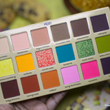 Makeup palette with various colors held by a hand against a blurred background
